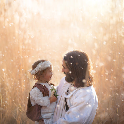 Jesus with a young child holding a flower and smiling.